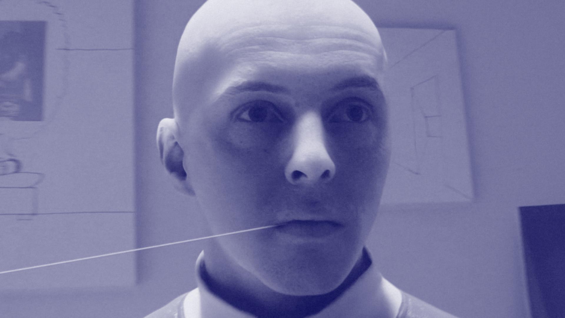 Zdjęcie portretowe, kadr z animacji. Głowa łysego mężczyzny, z nicią w ustach. W tle widać powieszone na ścianie szkice. | Portrait photo, frame from animation. The head of a bald man with a thread in his mouth. In the background you can see sketches on the wall.