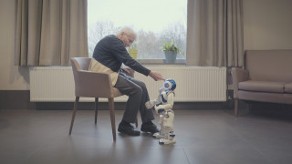 Starszy mężczyzna rozmawiający z robotem. | An elderly man talking to a robot.