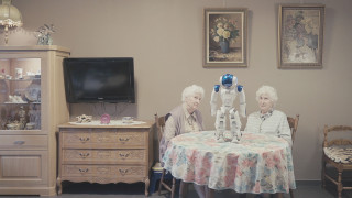 Siostry bliżniaczki siedzące przy stole i rozmawiające z robotem. | Twin sisters sitting at the table and talking to the robot.