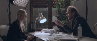 Zdjęcie przedstawiające dziennikarkę i naukowca siedzących przy stole. | Photo showing a journalist and scientist sitting at the table.