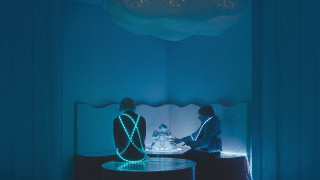 Ciemny pokój, rozświetlony delikatnymi, niebieskimi lampkami i dwie kobiety słuchające baśni opowiadanej przez robota. | A dark room, illuminated by delicate blue lamps and two women listening to a fairy tale told by the robot.