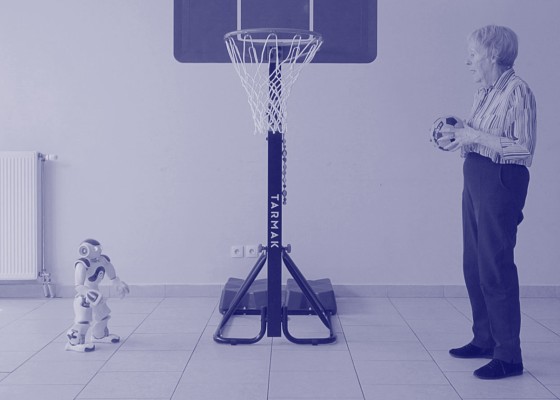 Starsza kobieta grająca z robotem w koszykówkę. | Elderly woman playing basketball with a robot.