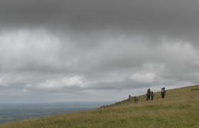 Zdjęcie przedstawiające bohaterów z dziećmi w oddali na zielonym wzgórzu. | A photo showing the heroes with children in the distance on a green hill.